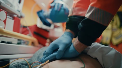EMS Paramedics Team Provide Medical Help to Injured Patient on the Way to Hospital. Emergency Care Assistants Using a Defibrillator and Ventilation Mask to Bring the Man Back to Life in an Ambulance.