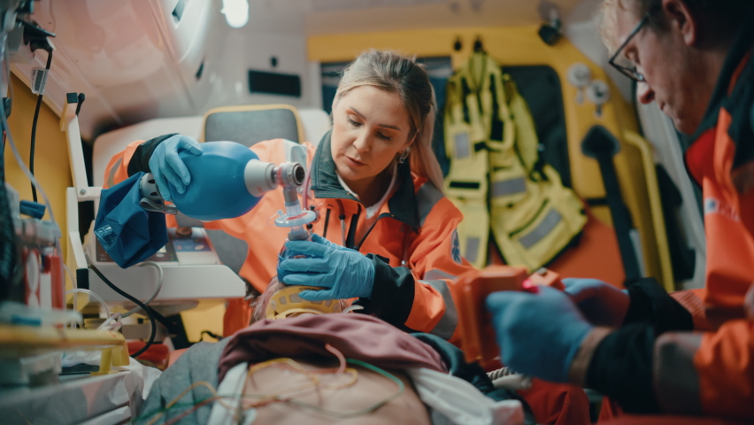 Female and Male EMS Paramedics Provide Medical Help to an Injured Patient on the Way to a Healthcare Hospital. Emergency Care Assistants Using a Non-Invasive Ventilation Mask in an Ambulance. | Shutterstock HD Video #1060859617