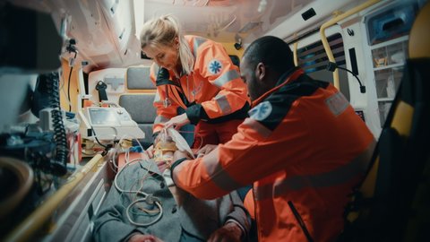 Female and Male EMS Paramedics Provide Medical Help to an Injured Patient on the Way to a Healthcare Hospital. Emergency Care Assistants Putting On Non-Invasive Ventilation Mask in an Ambulance.
