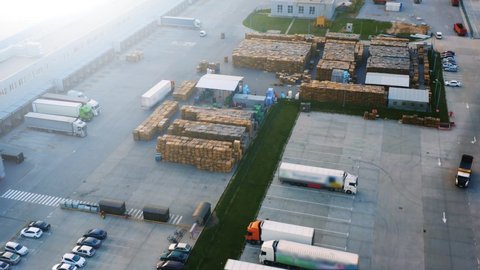 Aerial view of a semi trucks with cargo trailers standing on warehouses ramps for loading/unloading goods. Large logistics park with with a unsheltered warehouse for wooden pallets
