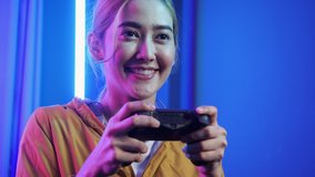 Asian young woman playing game online at home. Gamer girls controlling joystick for video game. Teenage girls leisure game in neon light room at home. Cyberpunk color.
