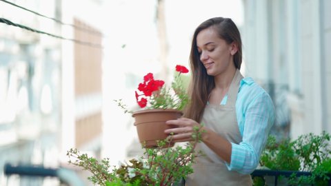Happy smiling cute woman gardener wearing apron with flower pot petunia taking care about balcony plants  