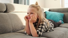 Little girl child watching TV at home lying on the couch. A kid watches cartoons and educational programs