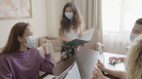 Modern international office. Workers and managers in medical masks working at laptop and discuss ideas. Good team work. Buisness during coronavirus pandemic covid. People giving high five.