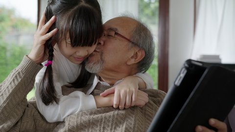 Close up old senior asian grandparent play and watch with kid grandchildren with technology on computer tablet at home in bonding relationship in family. Young girl hug older man from back. Stock-video