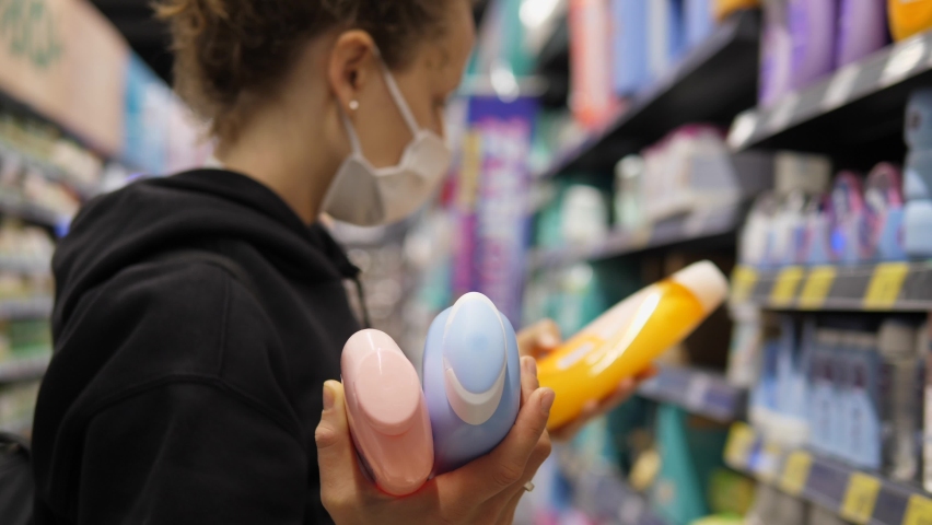  Shopping during covid 19 outbreak. Caucasian woman in face mask comparing beauty care products in store Royalty-Free Stock Footage #1060867327