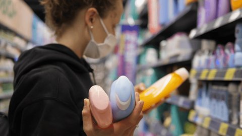  Shopping during covid 19 outbreak. Caucasian woman in face mask comparing beauty care products in store