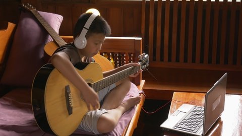 Young boy with a guitar plays the classical guitar. The asia child learns to play the guitar.