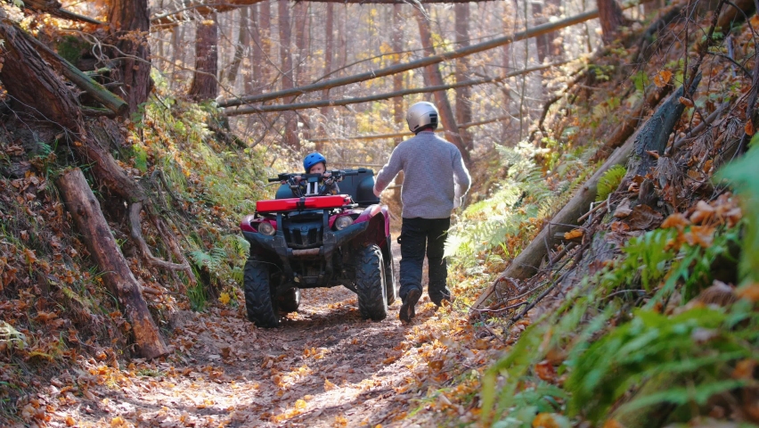 Outdoor activity - man climbs on the ATV with his son riding ATVs in the forest