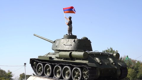 Girl and panzer.  Little girl with Artsakh flag staying on panzer. 
Face is not visible. Girl with flag on background blue sky.
