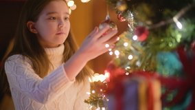 Happy little girl decorating christmas tree with balls. Lots of gift boxes under the tree. children decorating a Christmas tree. - Powered by Shutterstock - Get 15% off with code: PIKWIZARD15
