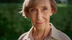 Closeup smiling senior woman posing at camera in summer garden. Senior lady looking down. Older woman turning head from camera. Female model standing outdoors alone - Powered by Shutterstock - Get 15% off with code: PIKWIZARD15