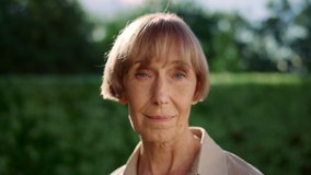 Closeup senior woman turning head to camera in slow motion. Portrait of mature woman posing at camera in park. Serious woman face expression. Older lady smiling at camera outdoors - Powered by Shutterstock - Get 15% off with code: PIKWIZARD15