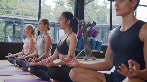 Group of diversity sporty in bodysuit relaxing meditation lotus pose by practicing yoga with instructor on mat floor at yoga class fitness gym. Multi racial group of women exercising healthy lifestyle