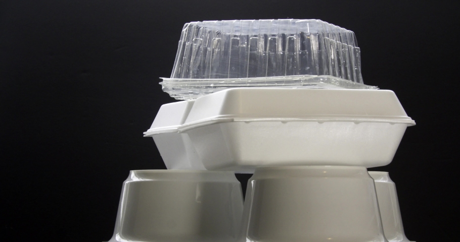 Front view of Styrofoam takeaway boxes, white foam boxes, rectangular shaped clamshell style container with an attached lid, on black background. Concept: single use containers.  Royalty-Free Stock Footage #1060881844