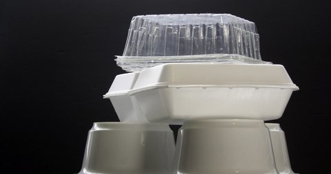 Front view of Styrofoam takeaway boxes, white foam boxes, rectangular shaped clamshell style container with an attached lid, on black background. Concept: single use containers. 