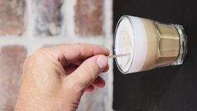 Cappuccino in a glass is stirred with a spoon, a man's hand is holding a spoon, close-up. The process of making mocha in a cafe. vertical layout