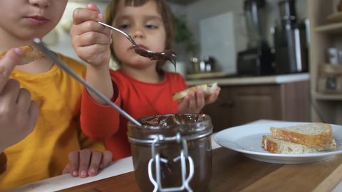 Children eat chocolate paste with a spoon from a jar at the table at home in the kitchen