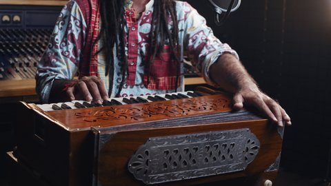Music production studio. Creative world. man playing harmonium in the sound studio. A long hair brunette male person in a traditional shirt plays meditation music.
