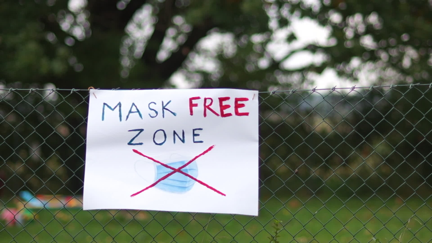 Poster on the fence with the inscription Mask Free Zone. Used surgical protective masks hang nearby. Protest against wearing masks, Anti-mask concept Royalty-Free Stock Footage #1060885477