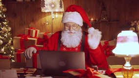 Happy Santa Claus holding gift box video calling kid talking to child in virtual video online chat meeting on laptop sit at home table late with present on xmas eve. Merry Christmas social distance.