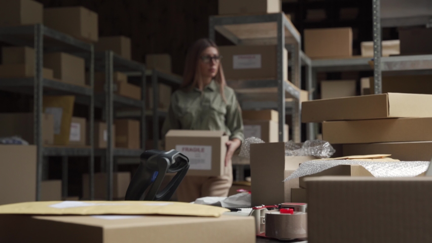 Female post mail storage worker holding tape dispenser sealing shipping online store order courier delivery cardboard box packing ecommerce fragile dropshipping parcel in distribution warehouse. Royalty-Free Stock Footage #1060892458
