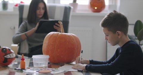 Kid drawing halloween holiday decoration with pencils. Young mother working at home. Social media campaign for pandemic coronavirus covid-19 prevention.