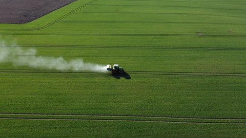 Farm tractor spreading fertilizers on early spring green crop field, aerial view