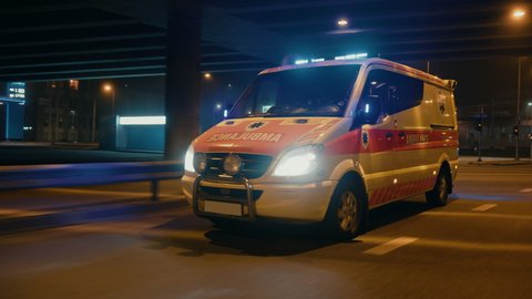 Parallel Moving Footage of an Ambulance Vehicle with Working Strobe Light and Signal Driving to Emergency Call on a City Urban Street at Night. Emergency Paramedics Rescue Van with Medical Cross Logo.