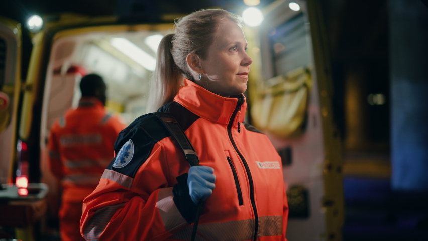 Portrait of a Female EMS Paramedic Proudly Standing in Front of Camera in High Visibility Medical Orange Uniform with "Paramedic" Text Logo. Successful Emergency Medical Technician or Doctor at Work. Royalty-Free Stock Footage #1060901125