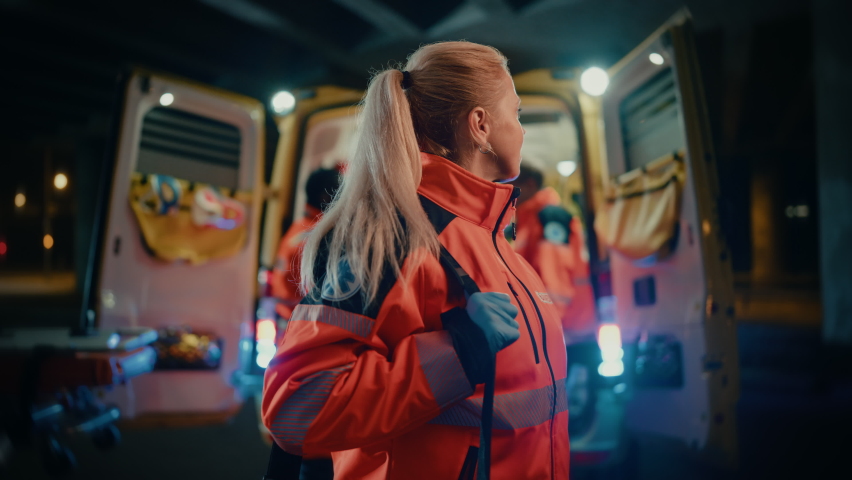 Portrait of a Female EMS Paramedic Proudly Standing in Front of Camera in High Visibility Medical Orange Uniform with "Paramedic" Text Logo. Successful Emergency Medical Technician or Doctor at Work. Royalty-Free Stock Footage #1060901128