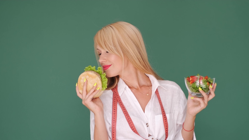 Junk food and healthy. Vegeterian woman holding burger and bowl of fresh salad choosing healthy food. Dieting concept.