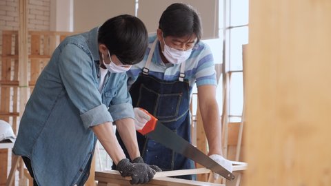 Asian man carpenter training showing apprentice how to use hand sawing in the workshop.