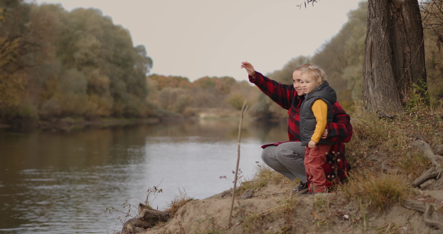 happy family weekend at autumn, woman with little child are enjoying forest landscape with lake, mother is educating little son