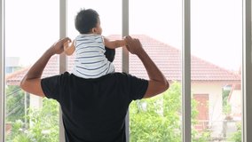 Asian happy newborn baby sitting on father neck and looking to outside window together.Family and love concept.