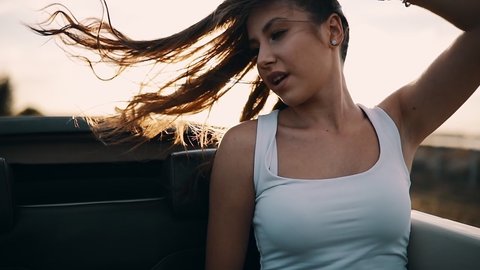 Young woman with open long hair in convertible at sunset