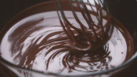 Chocolate. Mixing melted liquid premium dark chocolate with a whisk. Close up of liquid hot chocolate swirl. Confectionery. Confectioner prepares dessert, sauce. Slow motion