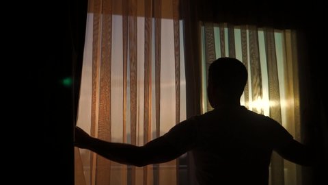 Cinematic Young Man Draws Curtains Open At Sunrise