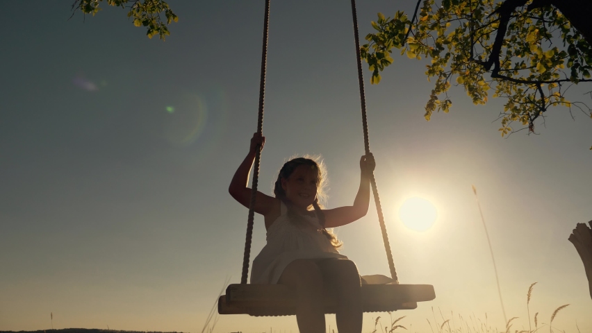 Amusement park dream concept. Happy girl swinging on swing in park at sunset. Child plays with wooden swing childhood dream, airplane pilot flights to sky. Happy family. Girl swinging on swing in park Royalty-Free Stock Footage #1060914577