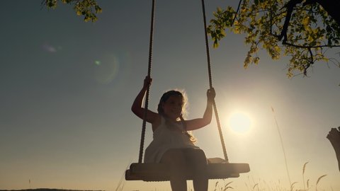 Amusement park dream concept. Happy girl swinging on swing in park at sunset. Child plays with wooden swing childhood dream, airplane pilot flights to sky. Happy family. Girl swinging on swing in park