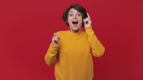 Young happy woman 20s years old in yellow sweater posing waiting for special moment worried making wish doing winner gesture say Yes isolated on red wall background in studio. People lifestyle concept