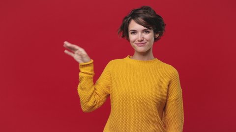 Smiling fun cute young woman 20s years old in yellow sweater posing isolated on red wall background in studio. People emotions lifestyle concept. Looking camera close her mouth lock and throw away key
