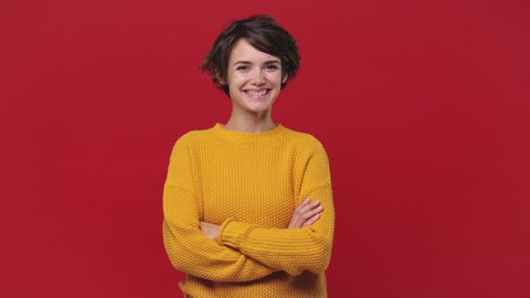 Smiling beautiful young woman girl 20s years old in yellow sweater posing isolated on red background in studio. People sincere emotions lifestyle concept Looking camera charming smile wink blink eye