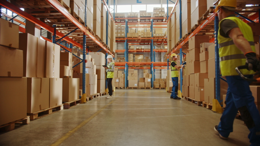 Retail Warehouse full of Shelves with Goods in Cardboard Boxes, Workers Scan and Sort Packages, Move Inventory with Pallet Trucks and Forklifts. Product Distribution Logistics Center. Ground Shot Royalty-Free Stock Footage #1060923340