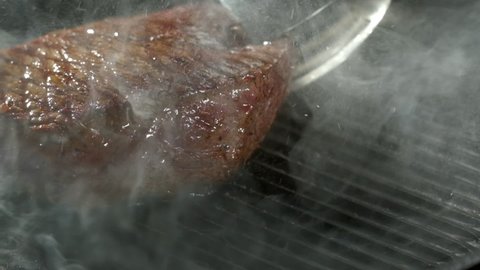 Pieces of juicy beef steak are fried in a grill pan. Close-up of the chef's hand slowly turning the pieces of meat