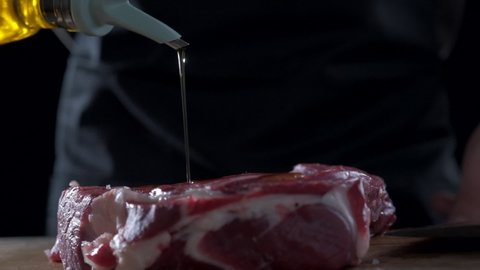 The chef pours olive oil over the meat for cooking, close-up.