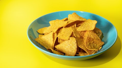Fried potato chips dissappearing from a blue plate on a yellow background. Stop motion.