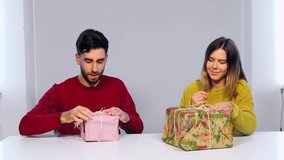 Woman and man sitting on the table and tearing up the wrapping paper on the present boxes. Christmas and New Year gifts.