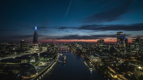 Revealing magically lit up green Tower Bridge, London Skyline, Establishing Aerial View Shot of London UK, United Kingdom, dusk early evening