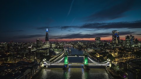 Revealing magically lit up green Tower Bridge, London Skyline, Establishing Aerial View Shot of London UK, United Kingdom, dusk early evening